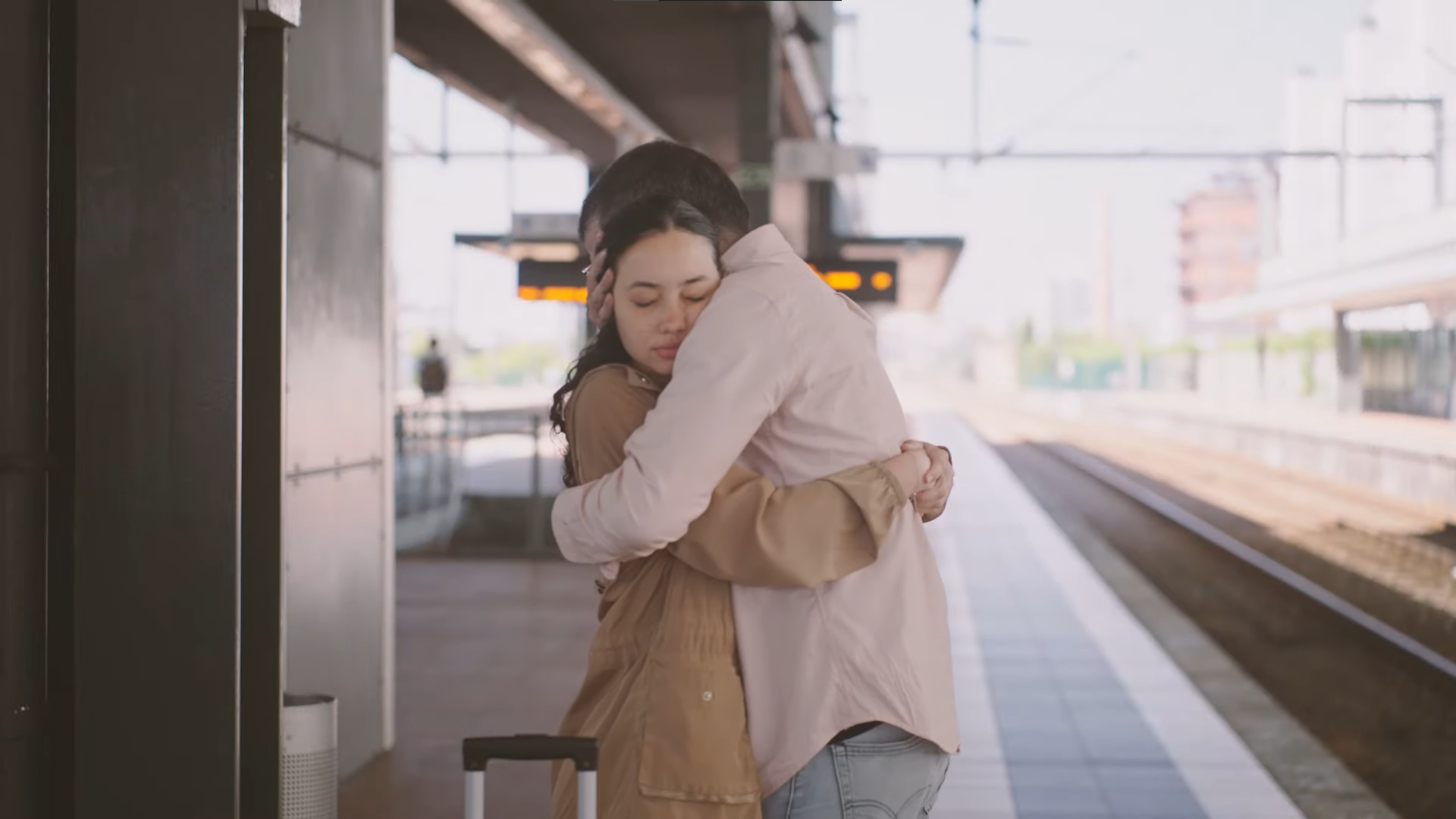 Uma rapariga e o seu pai estão abraçados na plataforma de uma estação de comboios.
